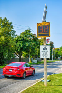 A red vehicle drives a by speed camera in a residential district.